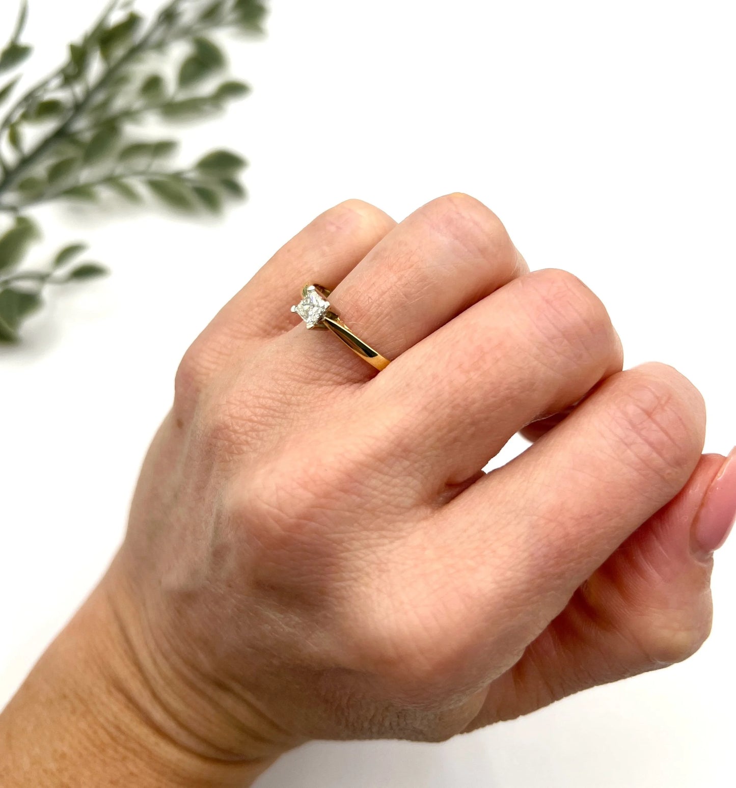 A solitaire princess cut diamond ring in yellow and white gold, modelled on a hand