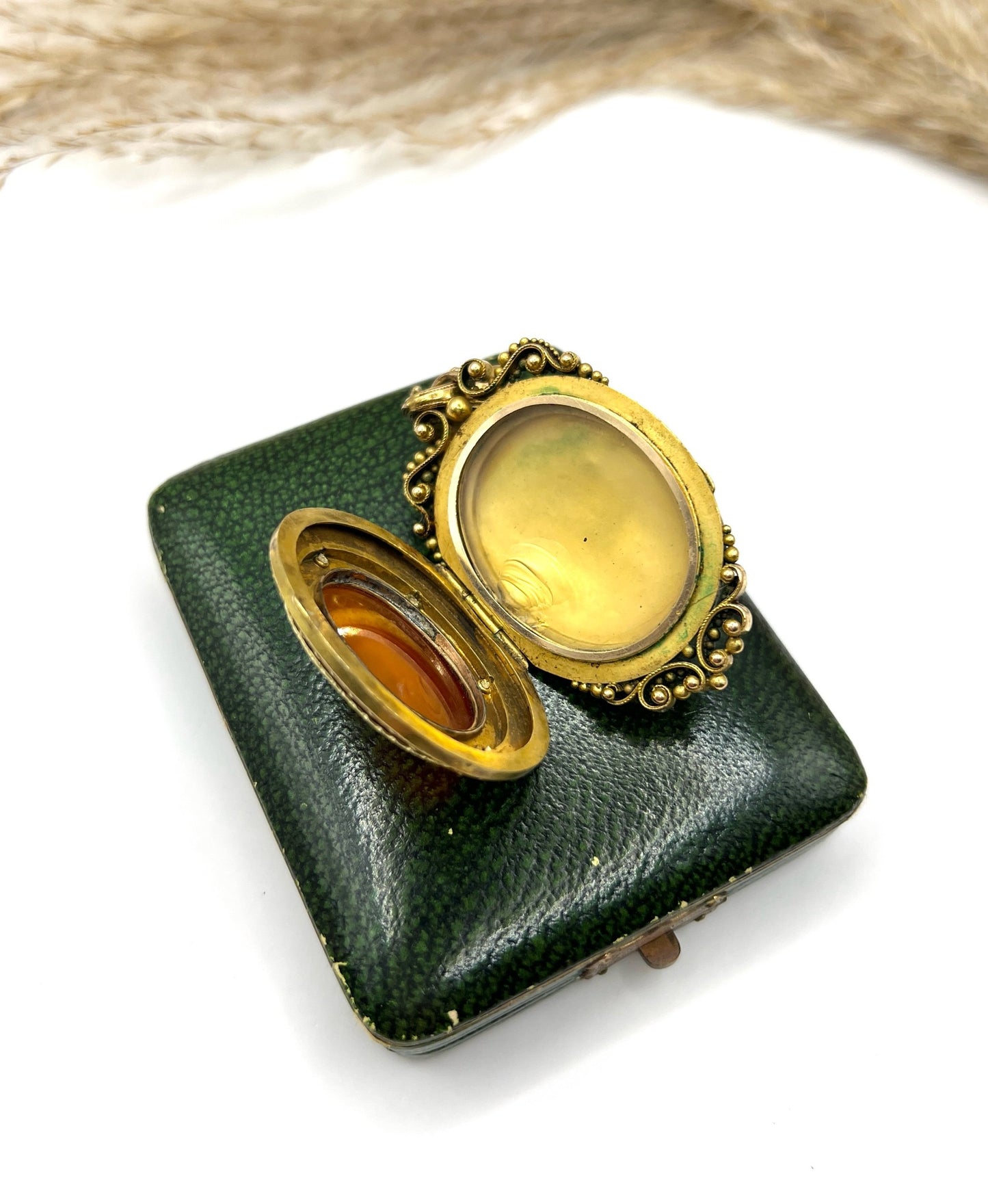 A yellow gold ornate locket pendant, open, on top of an antique box