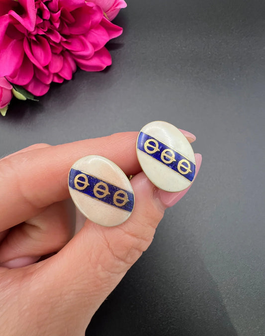 A pair of yellow gold enamel striped cufflinks with chain link fittings, held in a hand