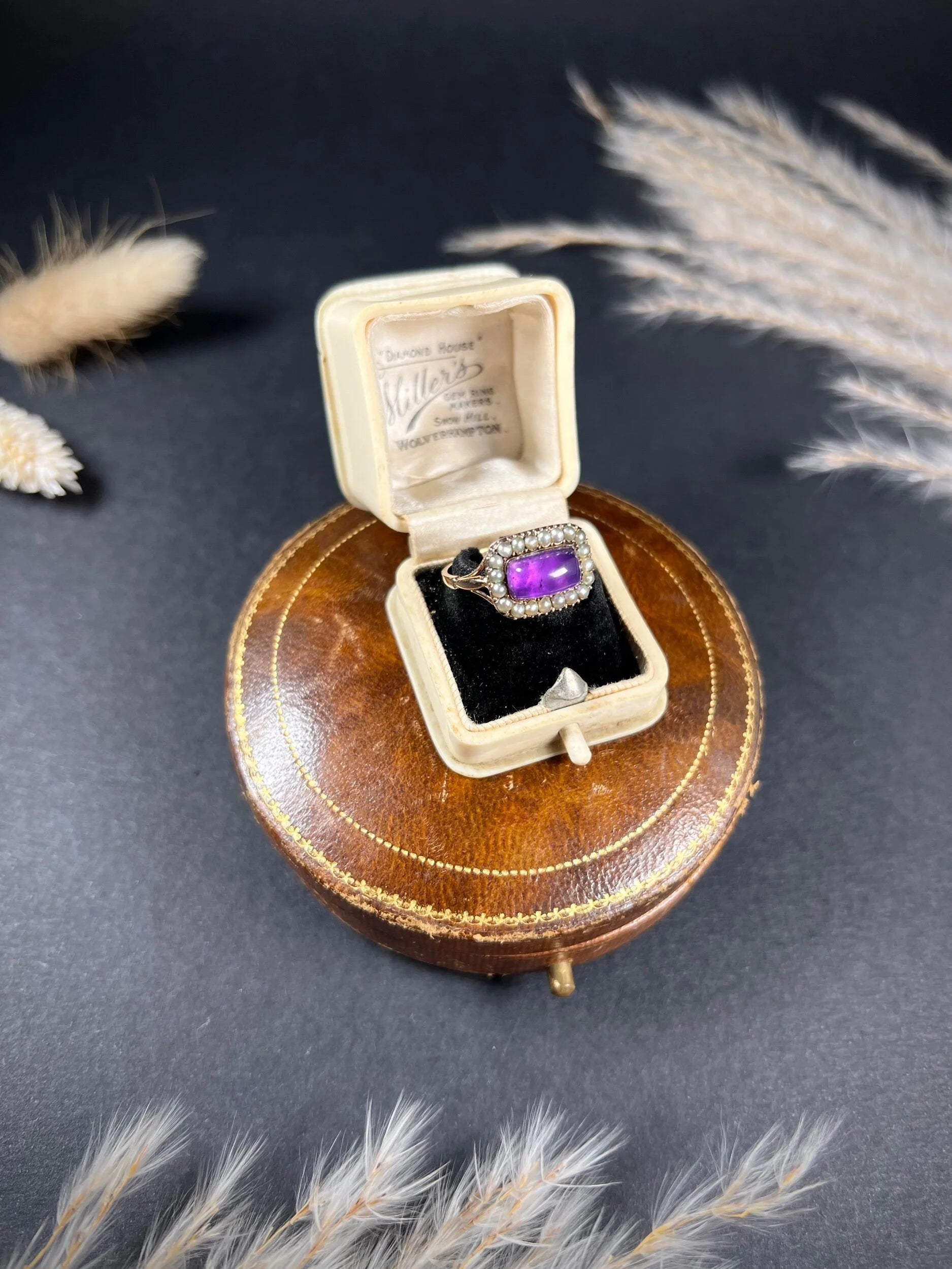A cabochon amethyst and pearl halo cluster ring in gold, in a ring box