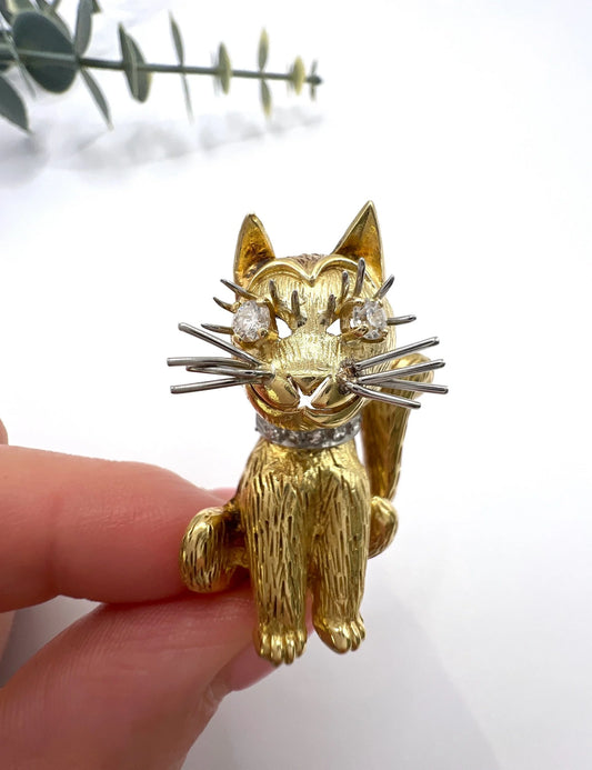 A yellow gold cat brooch with diamond eyes and collar, held in a hand