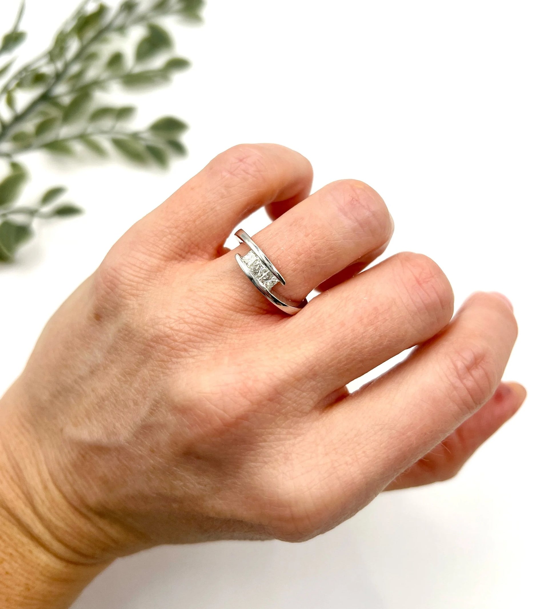 A three stone princess cut diamond crossover ring in white gold, modelled on a hand