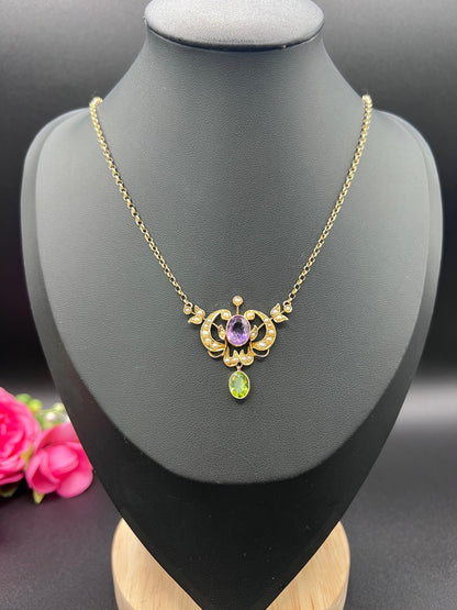 A yellow gold peridot, amethyst and seed pearl pendant necklace, on a black jewellery bust