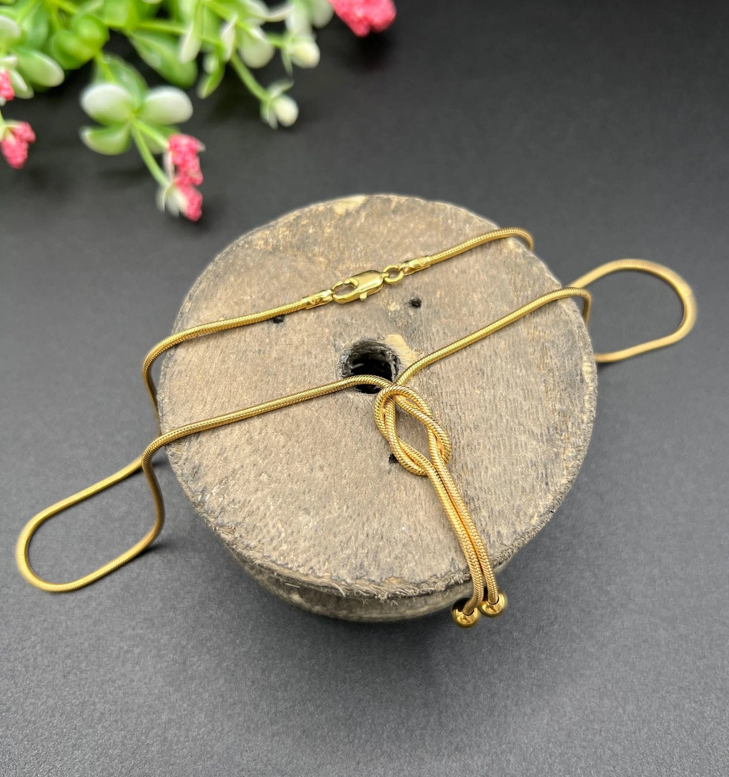 A yellow gold snake link chain necklace with a knot and tassel drop