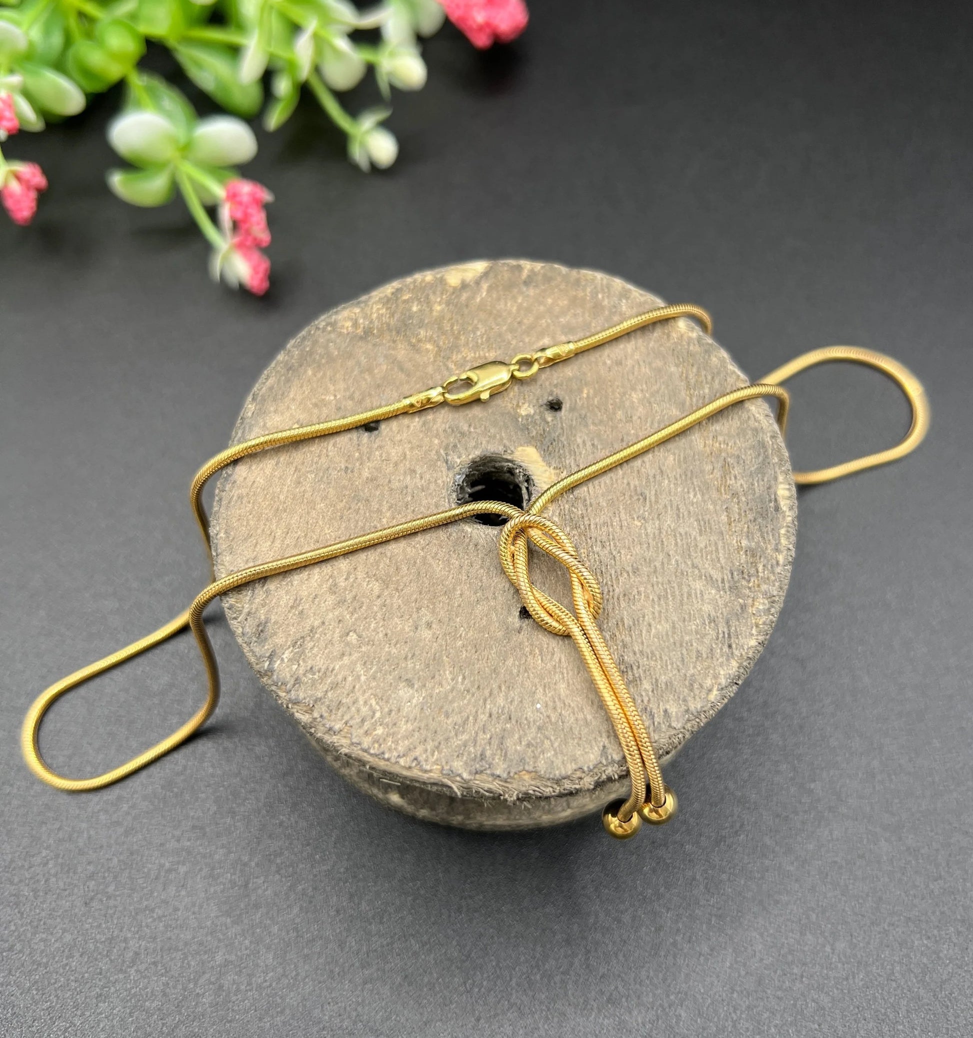 A yellow gold snake link chain necklace with a knot and tassel drop