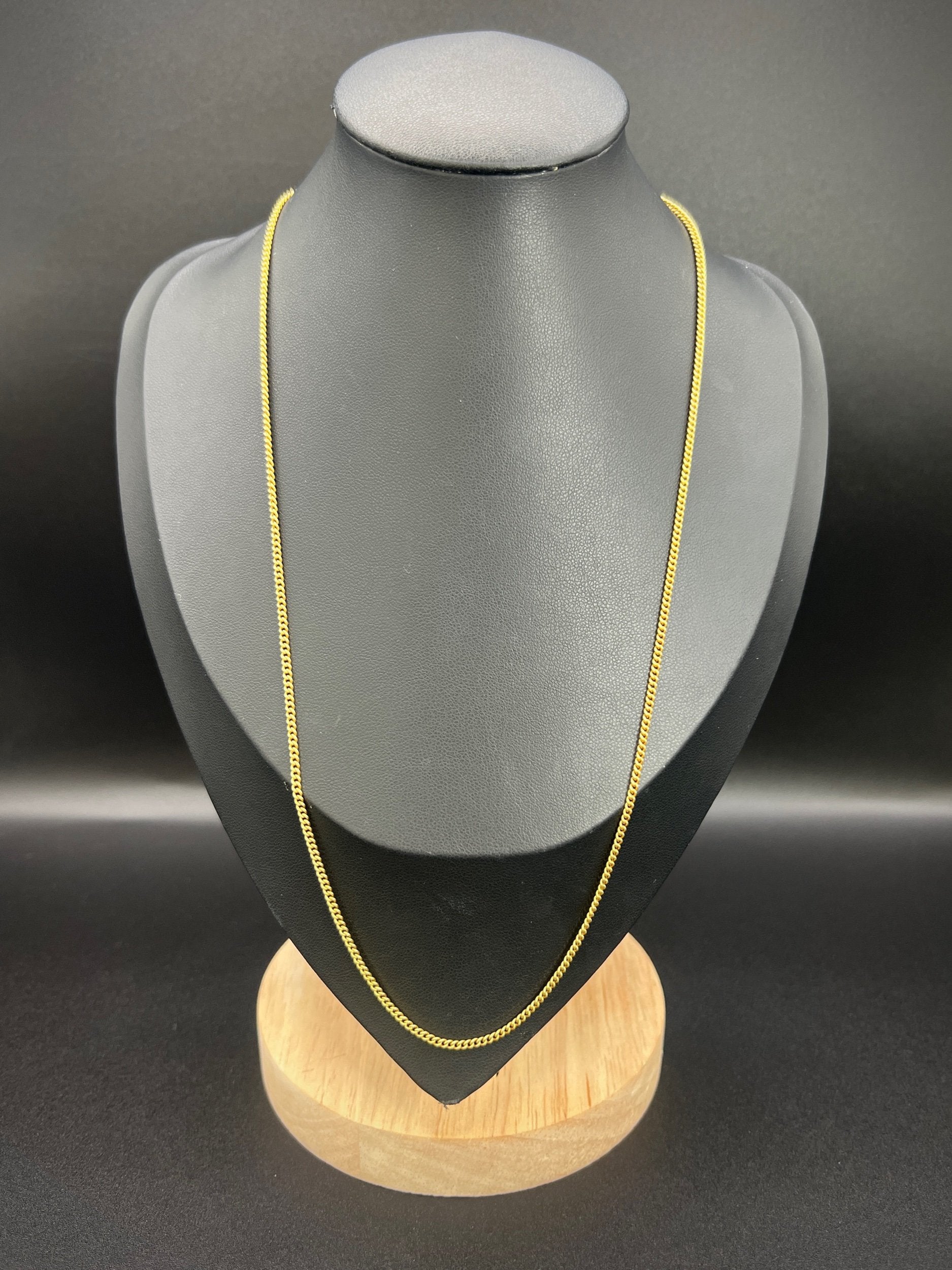 A yellow gold chain necklace, on a black jewellery bust