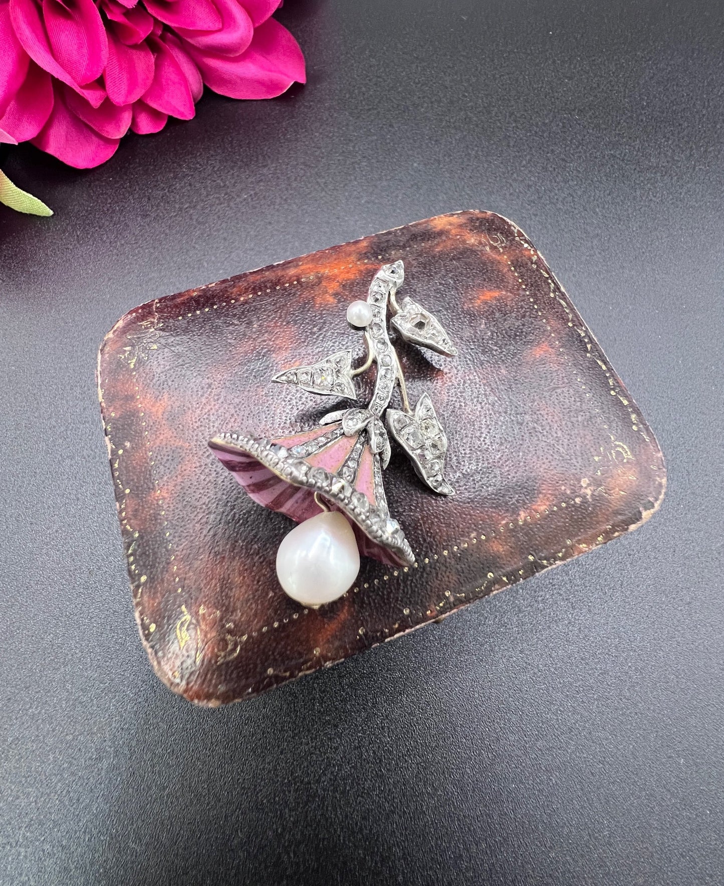 A pink enamel, diamond and pearl flower pendant in gold and silver, on an antique box