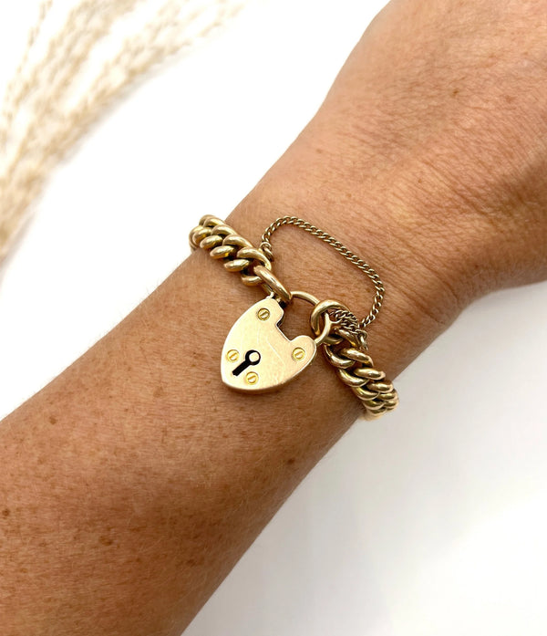 A gold curb link bracelet with heart shaped padlock, modelled on a wrist