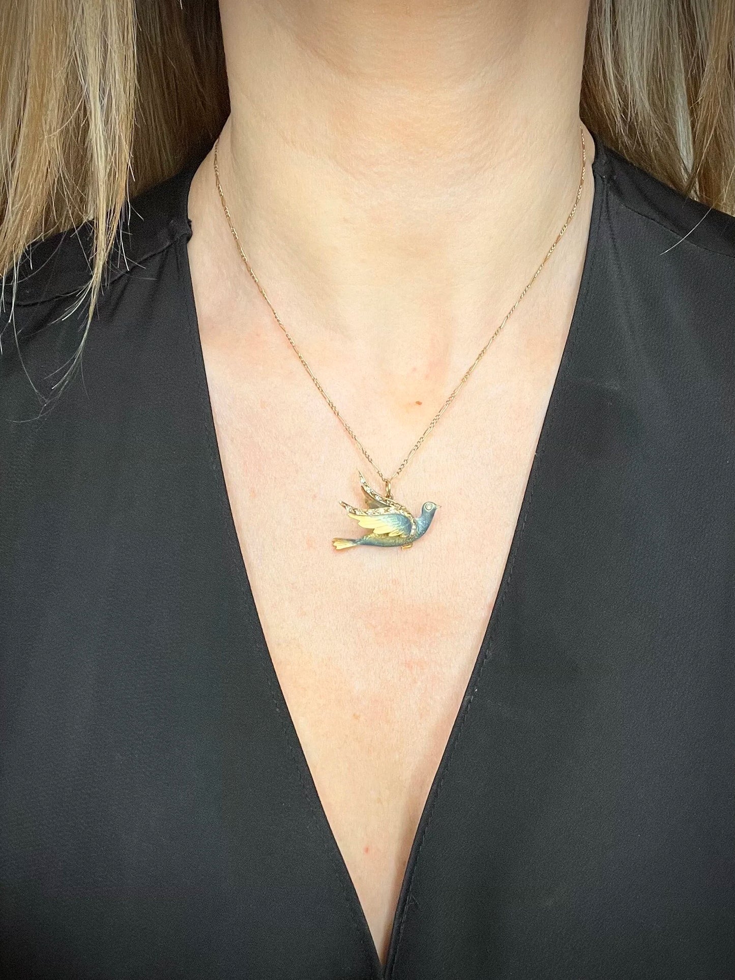 An enamel and diamond dove bird pendant, with a chain, modelled by a woman wearing a black top