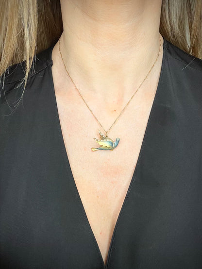 An enamel and diamond dove bird pendant, with a chain, modelled by a woman wearing a black top