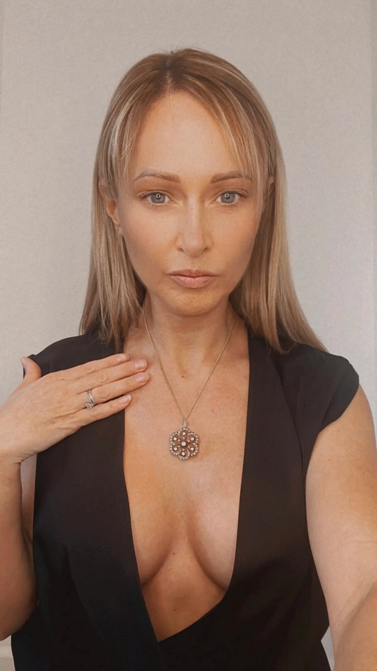 A floral design diamond set pendant/brooch with a gold chain, modelled by a lady wearing a black top