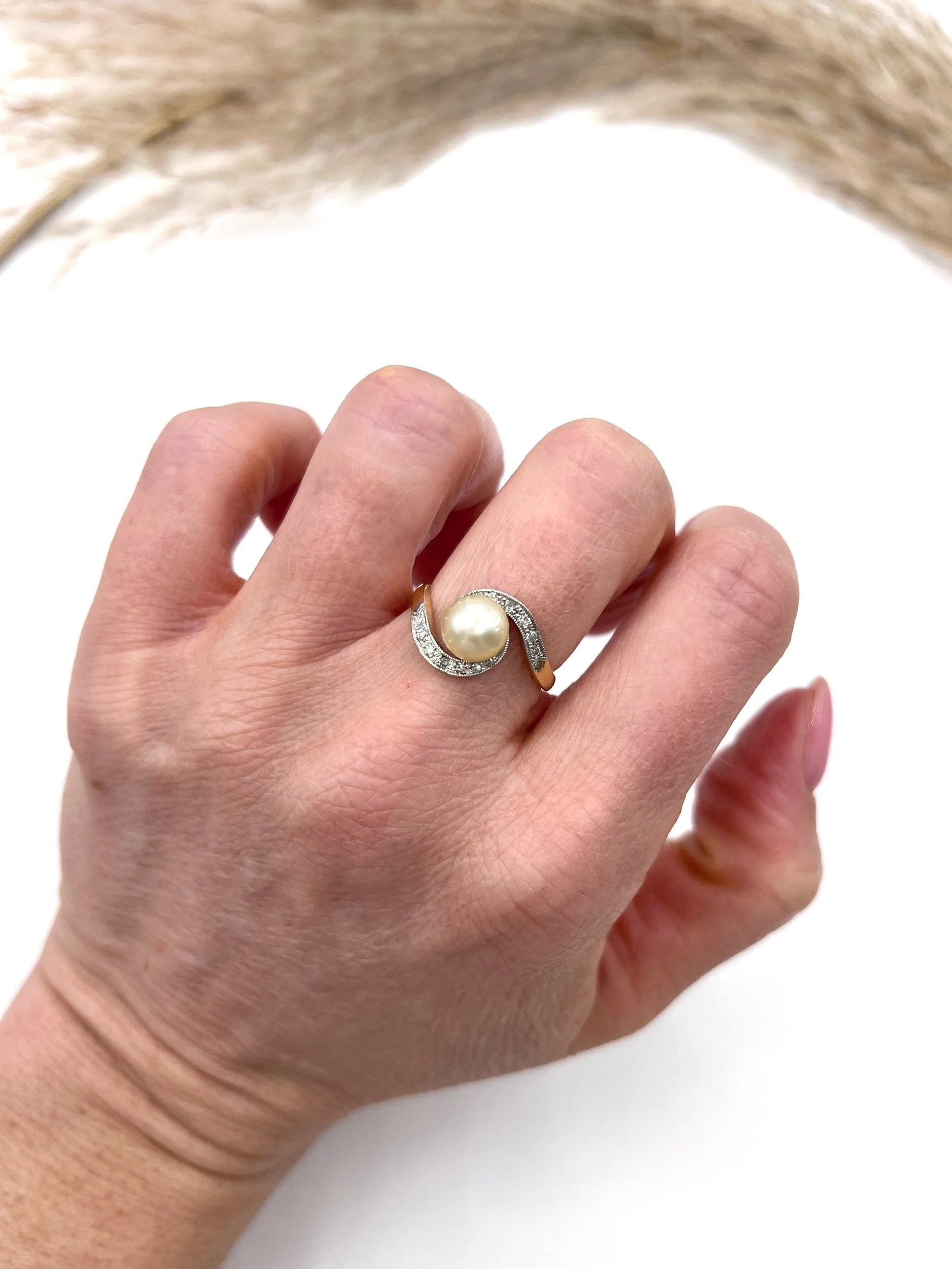 A pearl and diamond crossover swirl ring in yellow and white gold, modelled on a hand