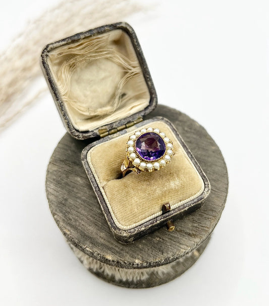 A cushion shaped amethyst cluster ring with a pearl border, in yellow gold, in a box