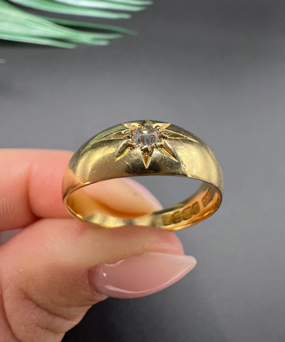 A single stone old cut diamond gypsy band ring in yellow gold, held in a hand