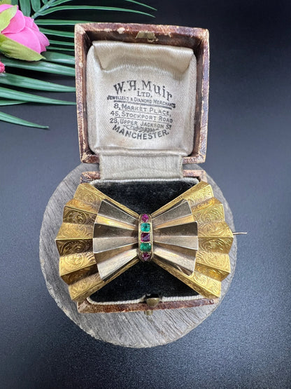 A yellow gold bow shaped brooch with rubies and emeralds