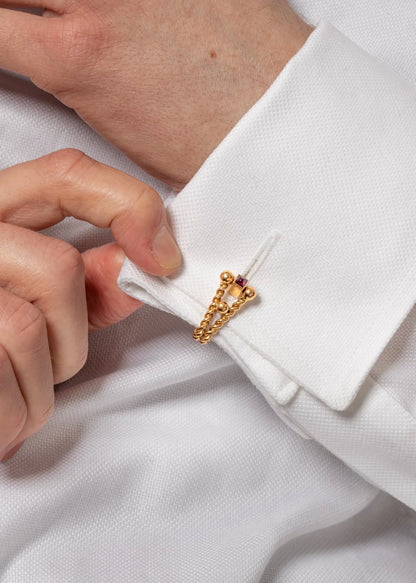 A gold ruby cufflink modelled in a white shirt cuff