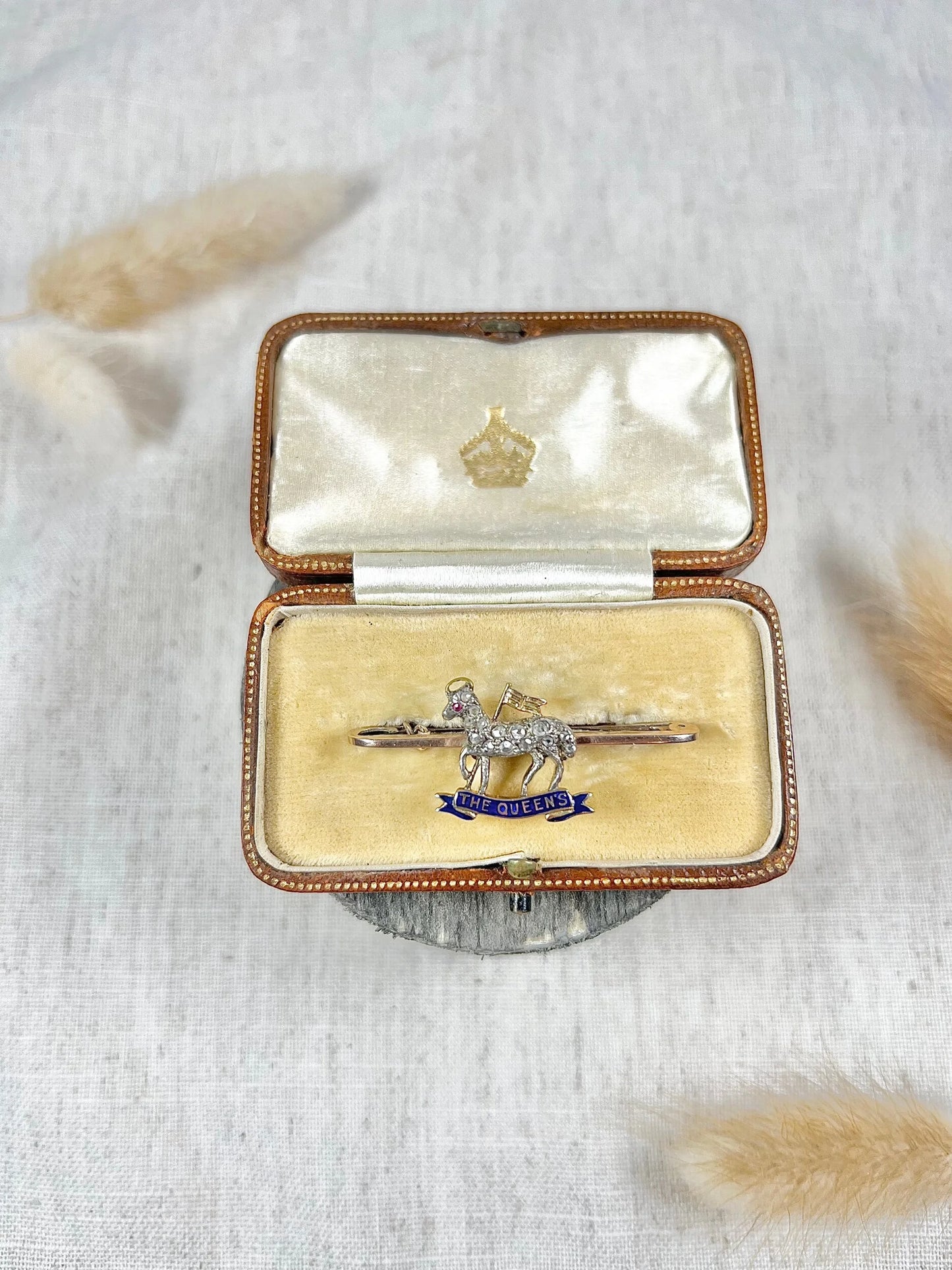 A diamond set regimental bar brooch in gold, with a blue enamel banner reading THE QUEEN'S, in an antique box