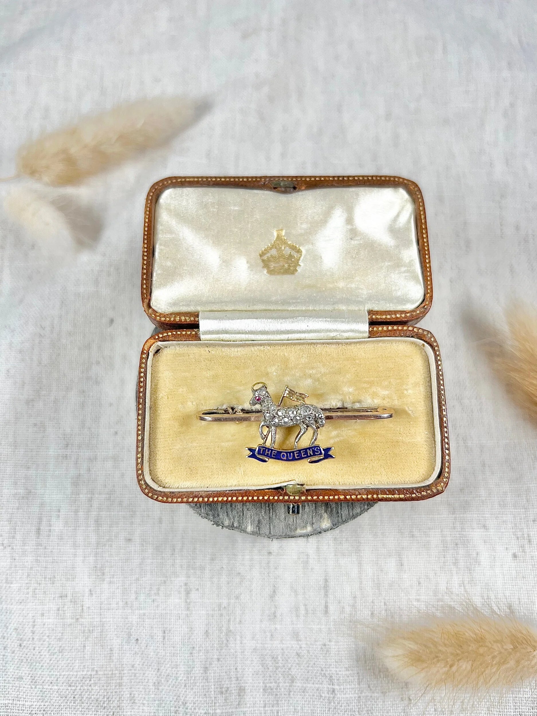 A diamond set regimental bar brooch in gold, with a blue enamel banner reading THE QUEEN'S, in an antique box