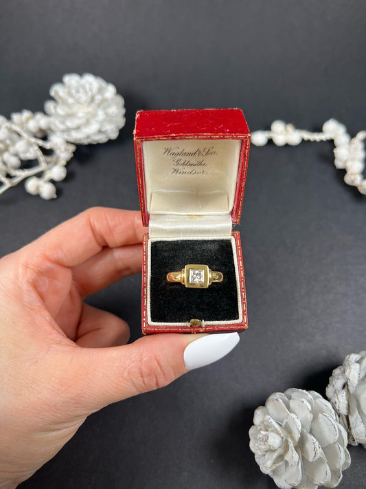 A yellow gold solitaire princess cut diamond ring, in an antique ring box held by a hand