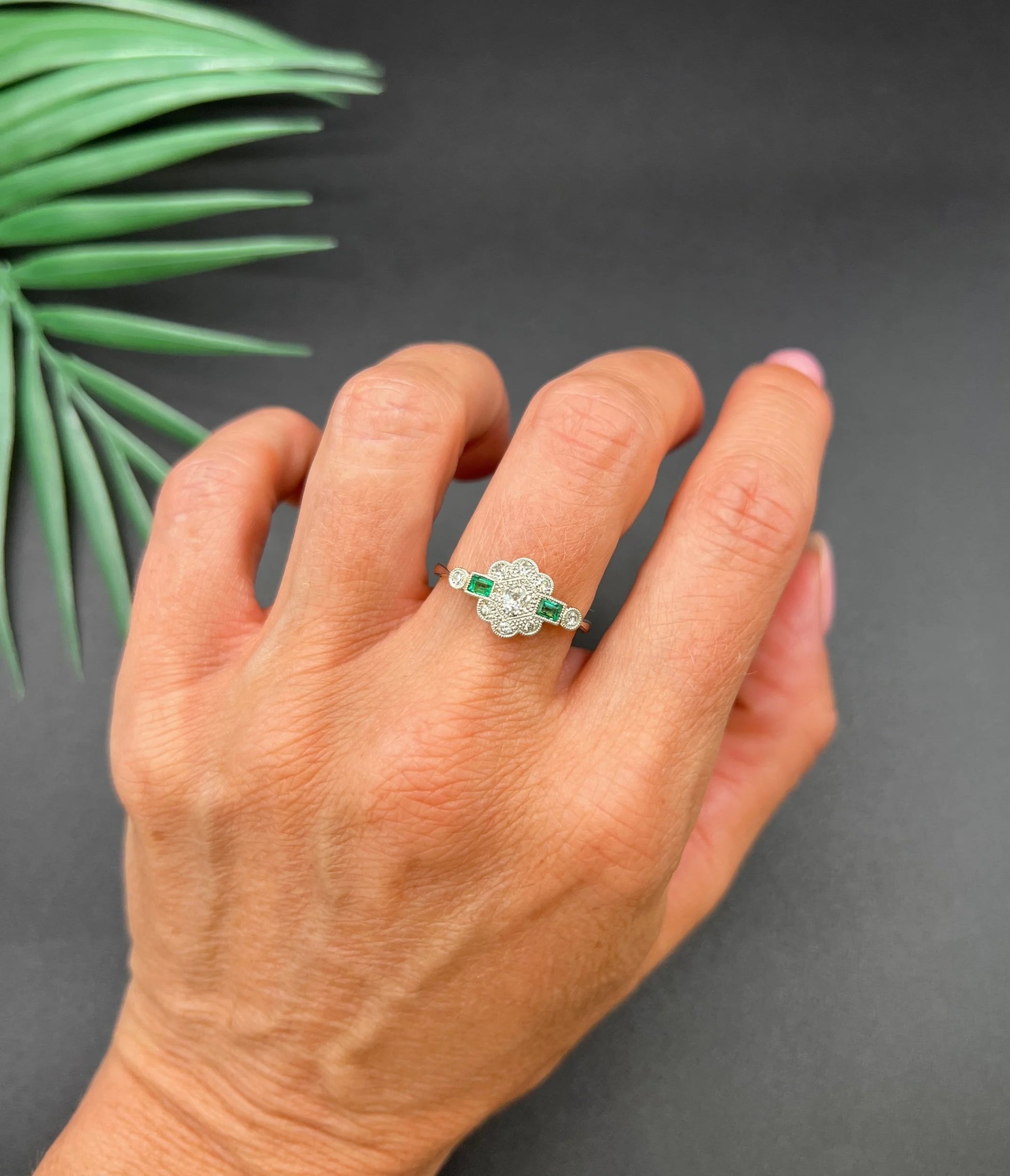 An emerald and diamond floral cluster ring in yellow gold and platinum, modelled on a hand