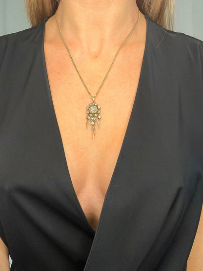 A yellow gold pendant with old cut diamonds, with a gold chain, modelled by a woman wearing a black top