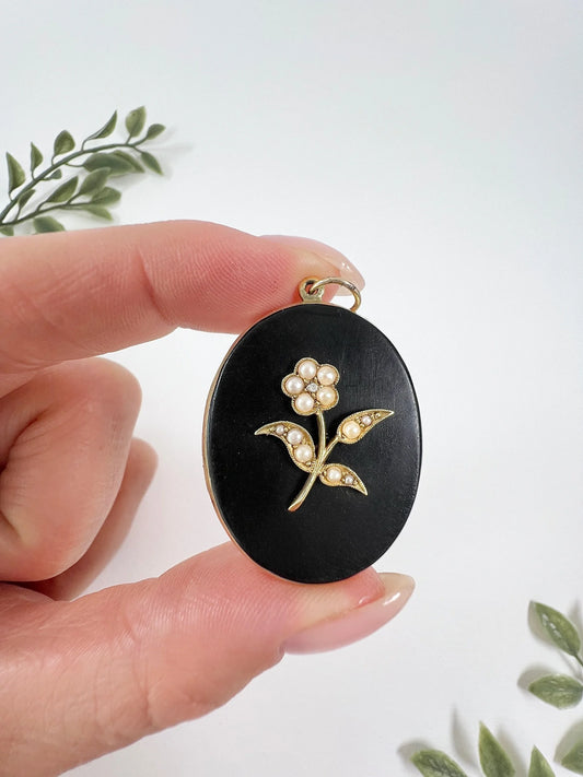 An oval onyx, pearl and yellow gold locket, held in a hand
