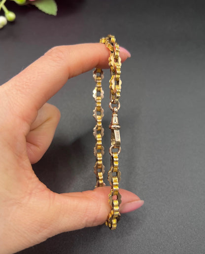 A fancy link yellow gold bracelet with a lobster claw clasp, held in a hand