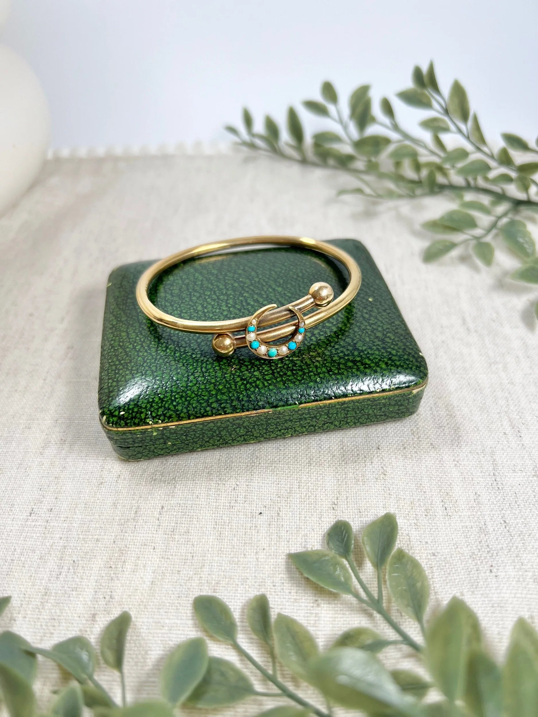 A yellow gold crossover bangle bracelet with a pearl and turquoise crescent moon centre