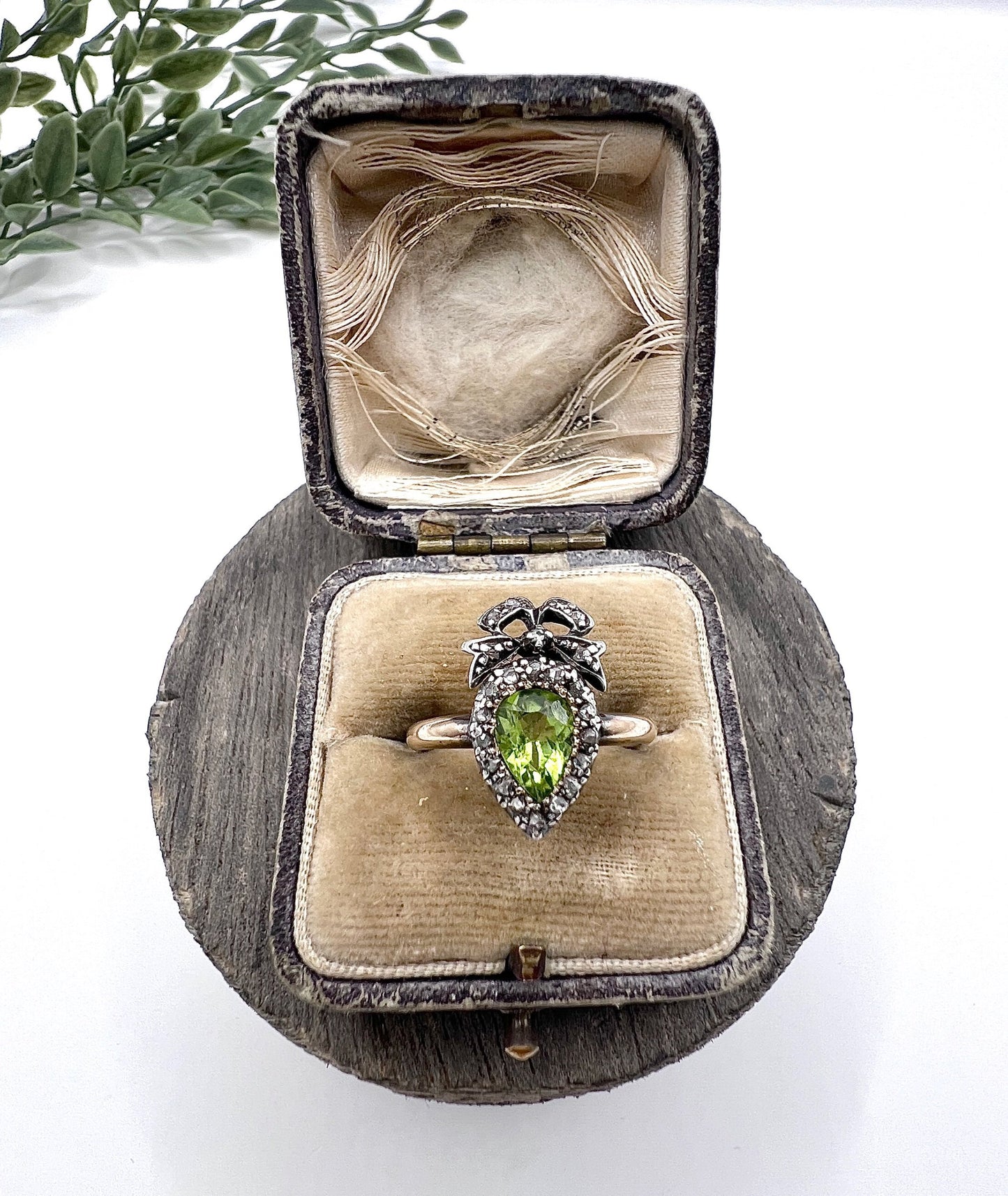 A pear cut peridot and round diamond cluster ring with bow detail, in yellow gold and white metal, in a ring box