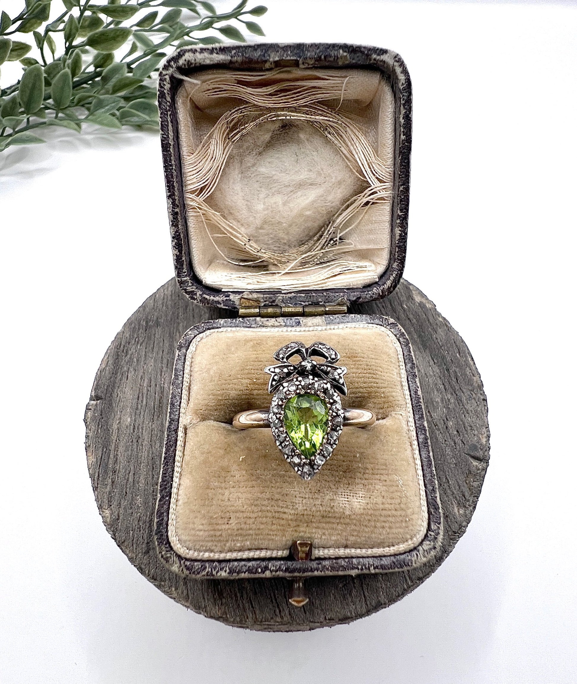 A pear cut peridot and round diamond cluster ring with bow detail, in yellow gold and white metal, in a ring box