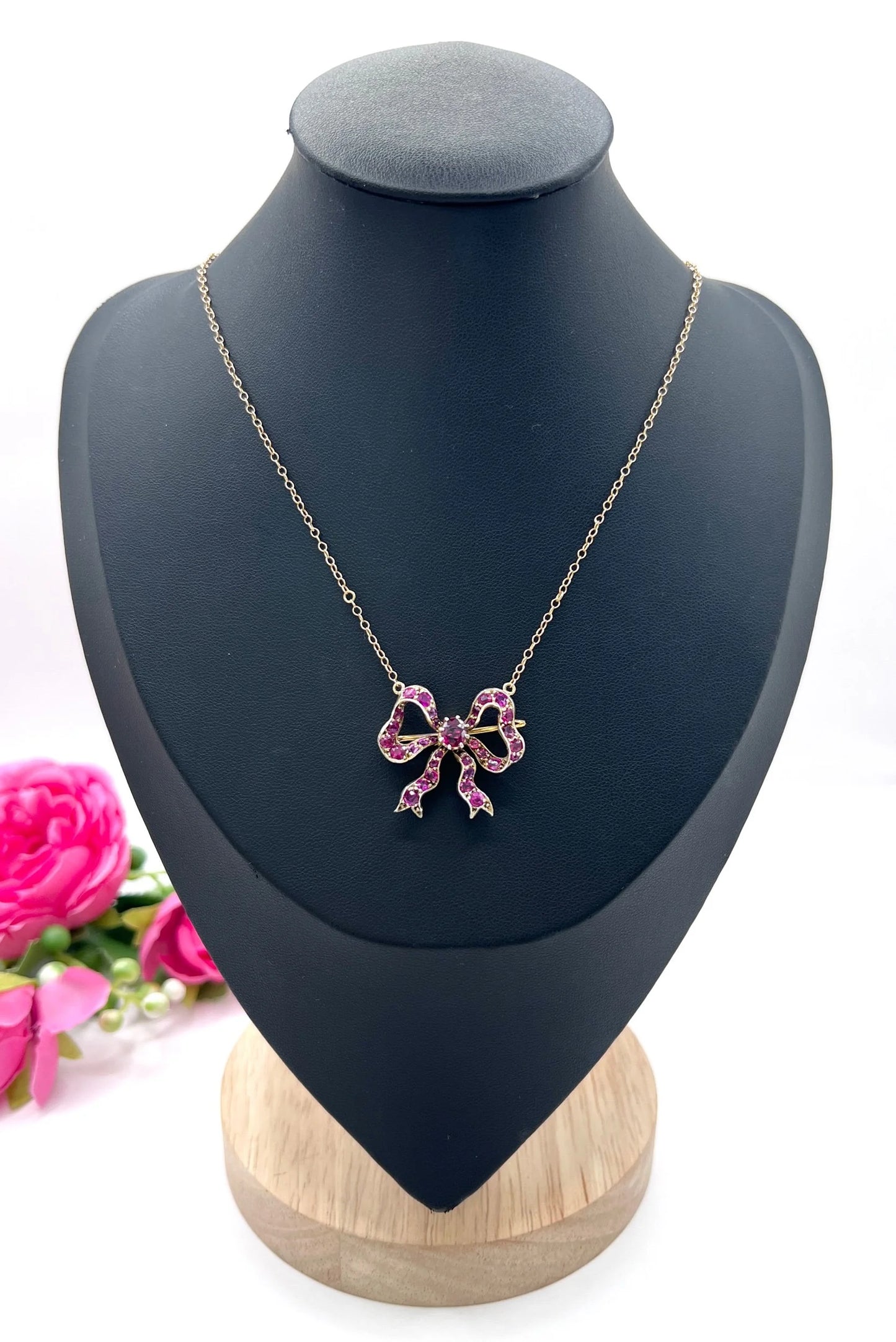 A ruby bow brooch necklace in gold and silver, on a black jewellery bust