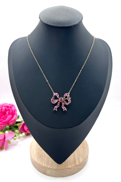 A ruby bow brooch necklace in gold and silver, on a black jewellery bust