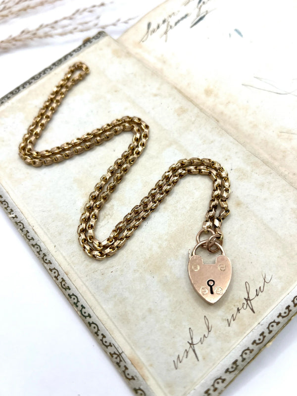 A gold chain necklace withgold heart padlock, on an antique book