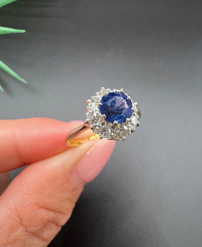 A circular cluster ring with sapphire and diamonds in yellow gold and platinum, held in a hand