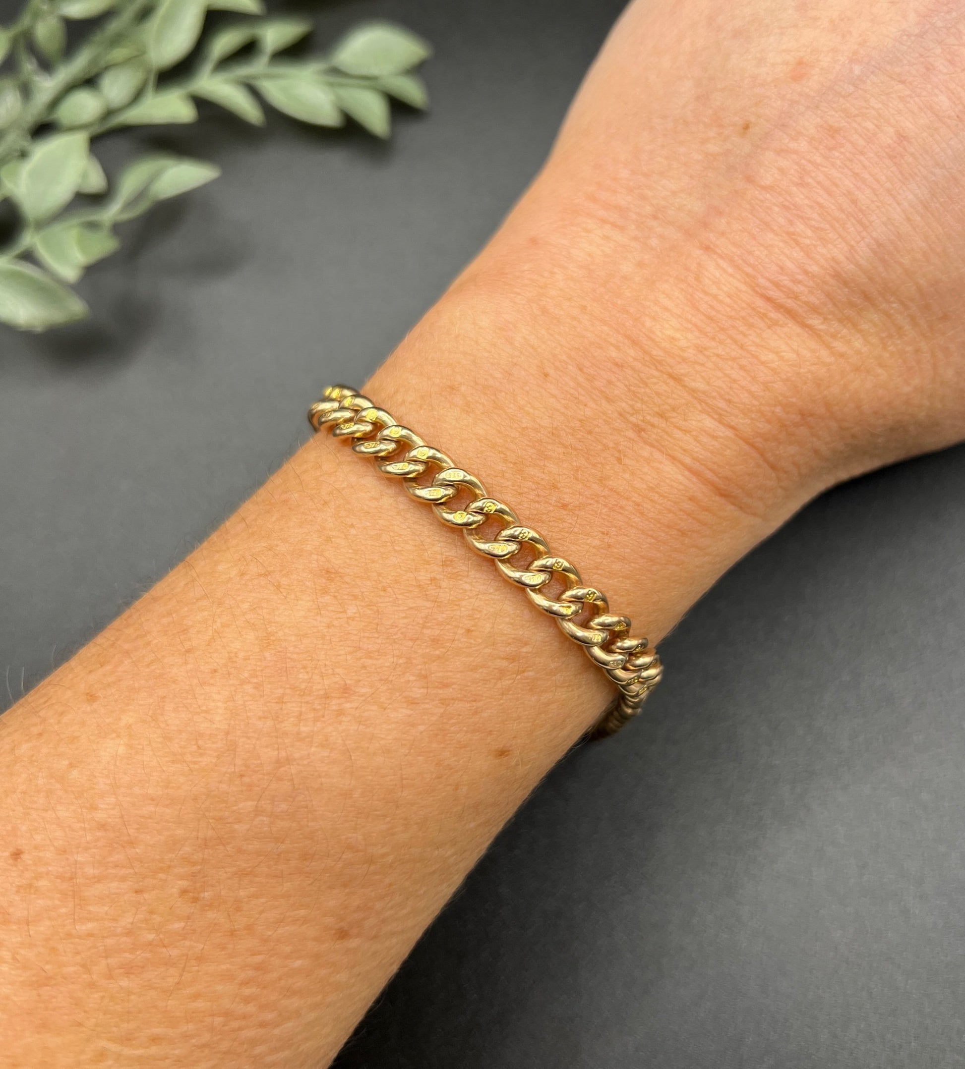 A gold curb link bracelet with a lobster claw clasp, modelled on a wrist