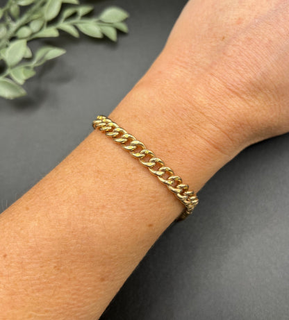 A gold curb link bracelet with a lobster claw clasp, modelled on a wrist