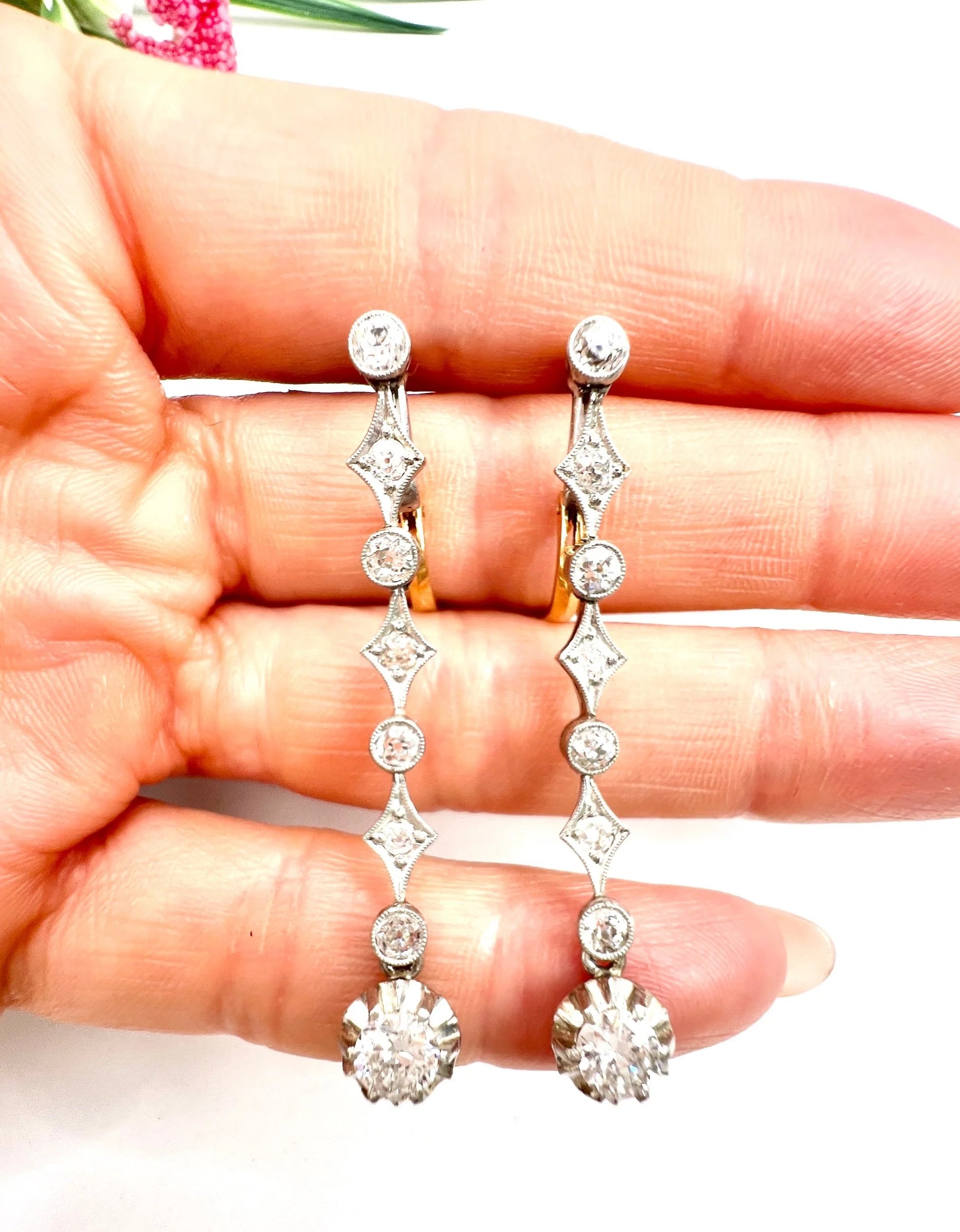 A pair of diamond drop earrings in yellow gold and platinum, held in a hand