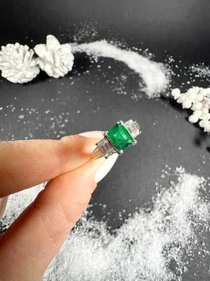 A three stone emerald and diamond ring in platinum, held in a hand