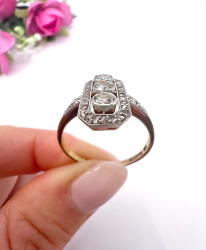 A diamond open cluster ring with three principal diamonds, in yellow and white gold, held in a hand