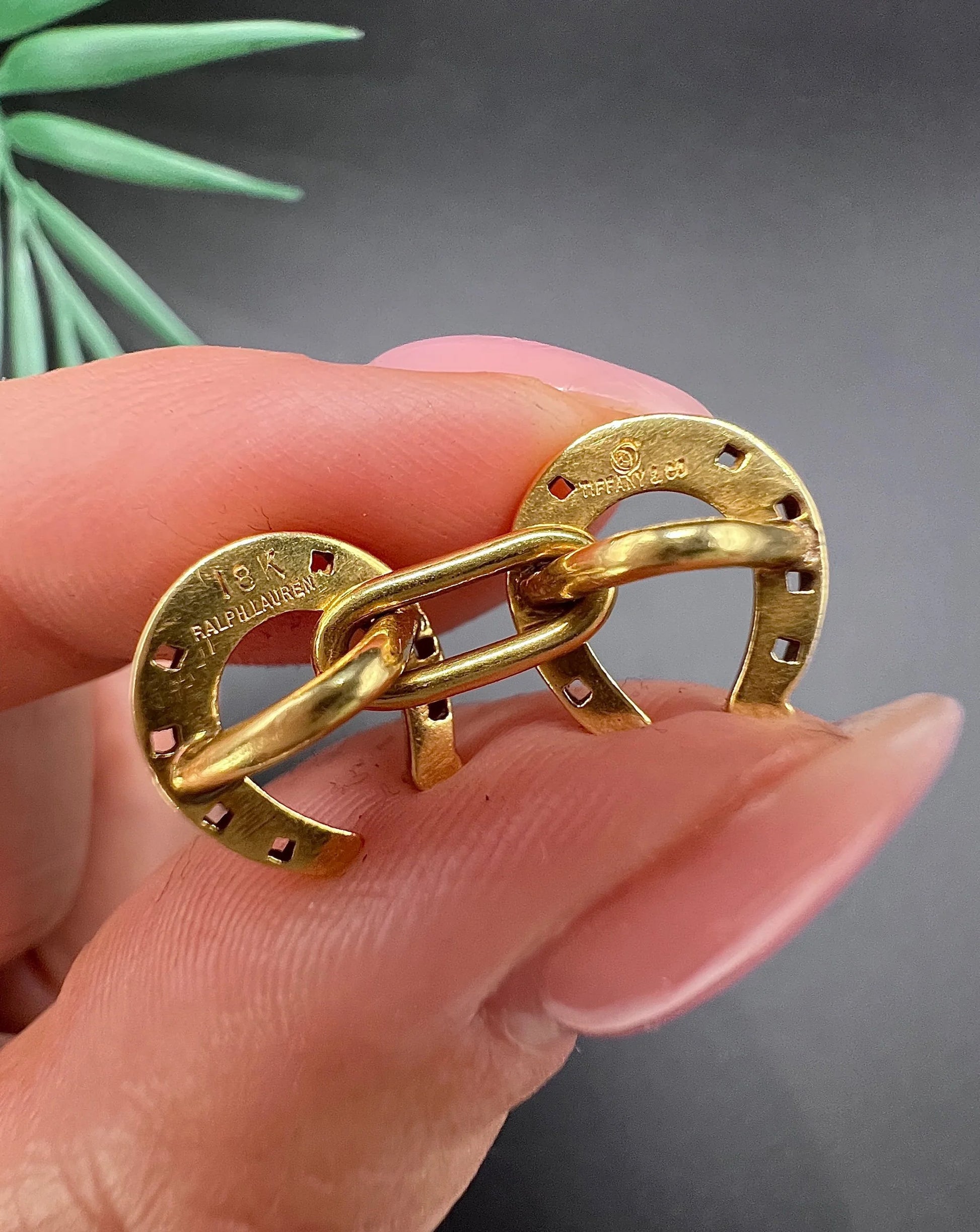 A double-sided horseshoe cufflink in yellow gold, held in a hand