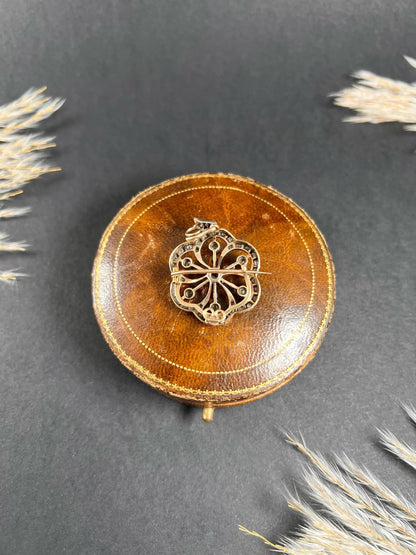 A floral design diamond set pendant/brooch on an antique brown jewellery box