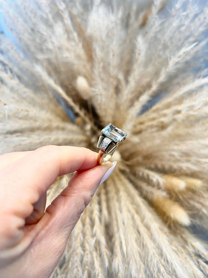 An aquamarine and diamond cocktail ring in gold, held in a hand