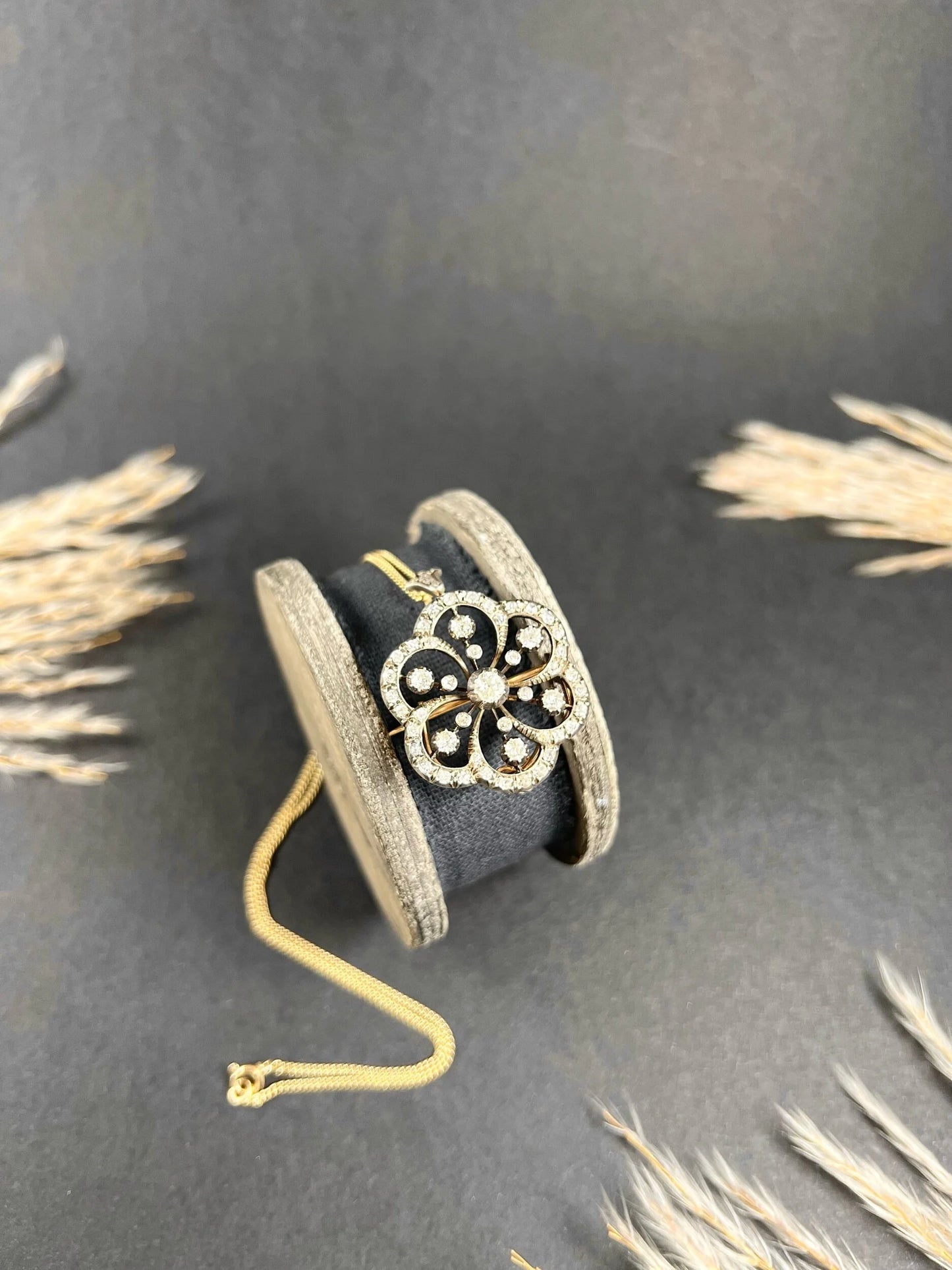 A floral design diamond set pendant/brooch, with a gold chain, on an antique box