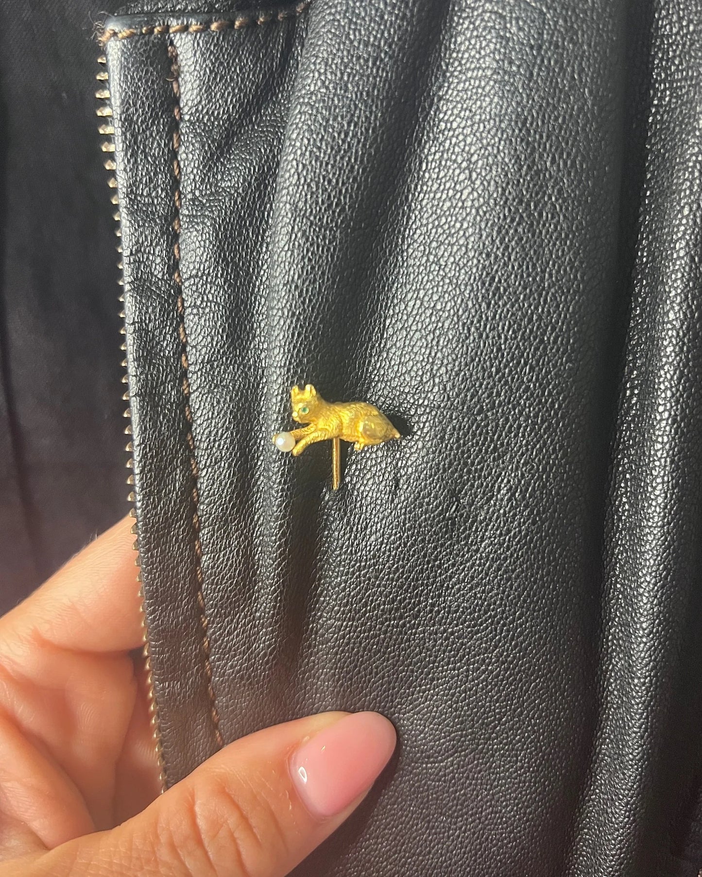 A yellow gold cat playing with a pearl ball stick pin, modelled on a black jacket