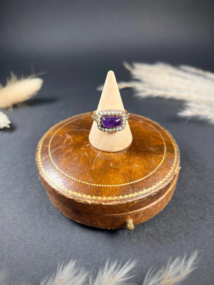 A cabochon amethyst and pearl halo cluster ring in gold, on a ring cone