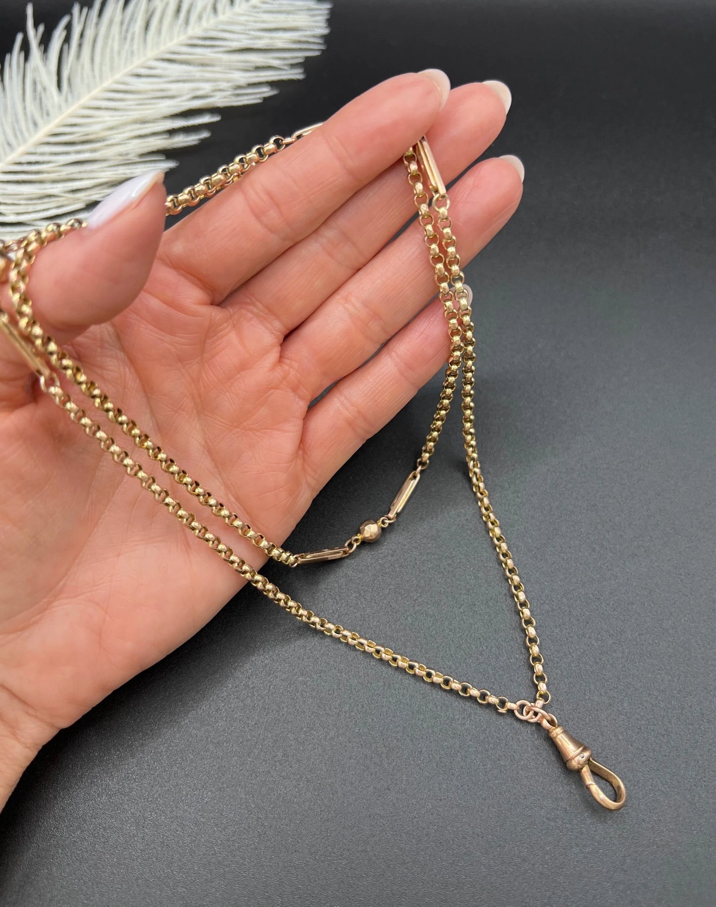 A long rose gold chain necklace with a dog clip clasp, held in a hand