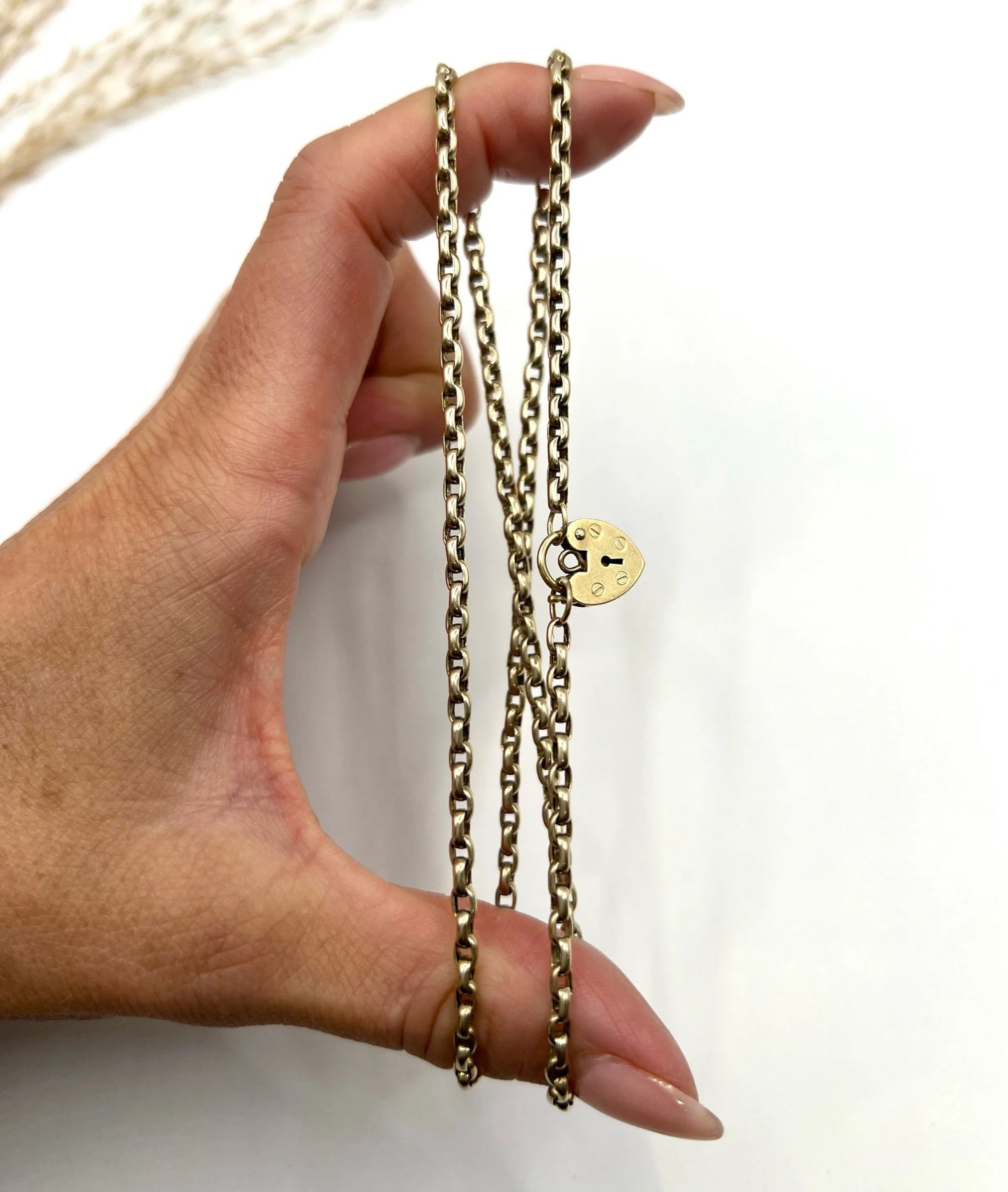 A gold belcher link chain with a heart shaped padlock clasp pendant, held in a hand