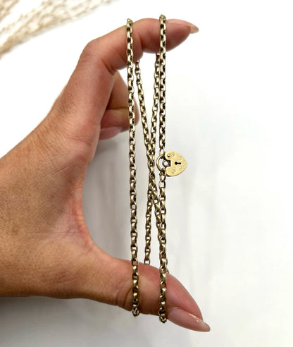 A gold belcher link chain with a heart shaped padlock clasp pendant, held in a hand