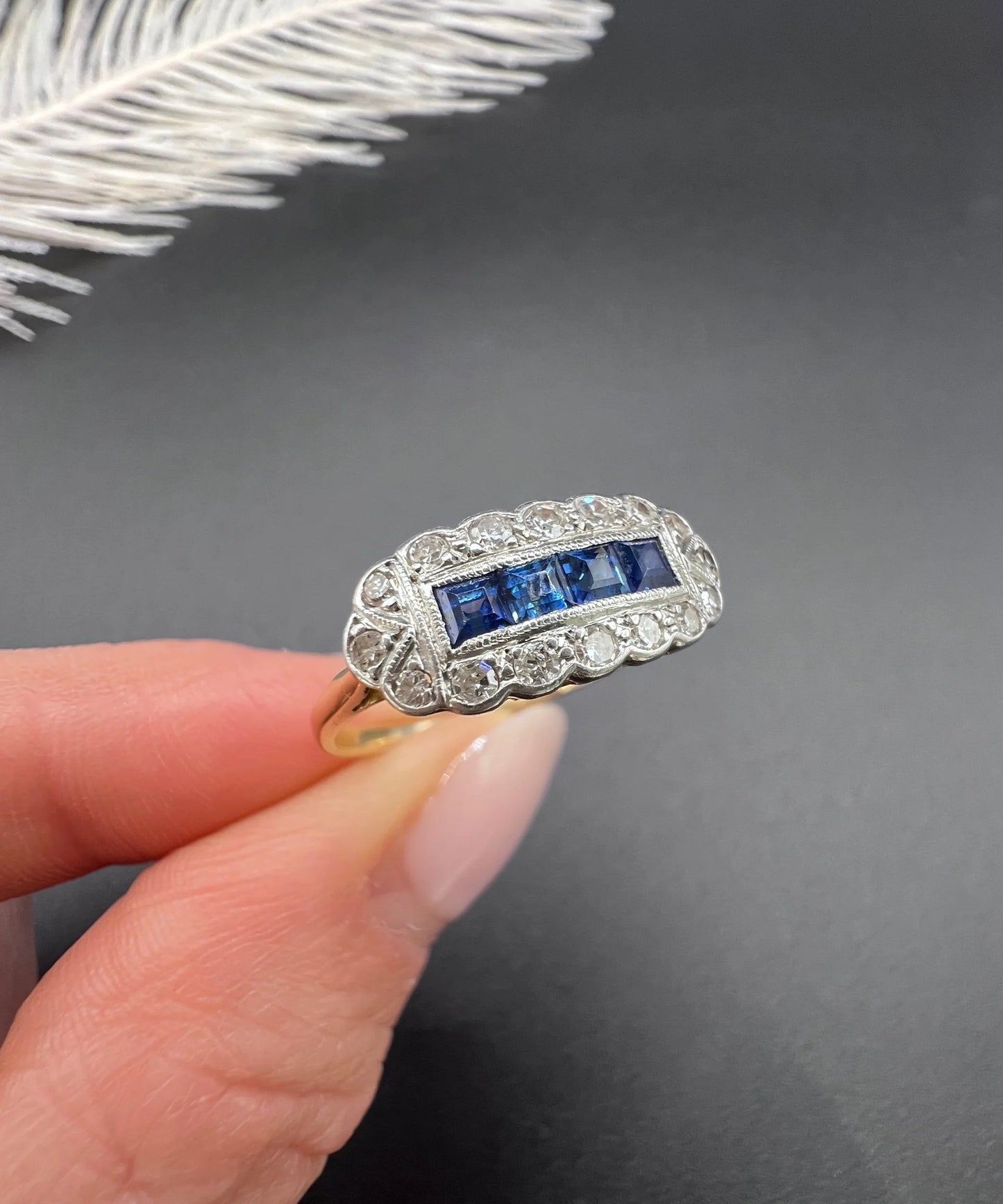 A sapphire and diamond elongated cluster ring in platinum and yellow gold, held in a hand