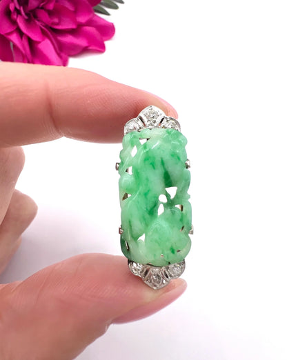 A carved green jade and diamond brooch in white gold, held in a hand